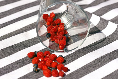 Raspberries, wild strawberries and blueberries fell from glass on tablecloth