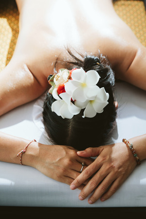 Beautiful woman having a wellness back massage with vintage film filter and spot lighting,Shallow depth of field with focus on flower overhead.の写真素材