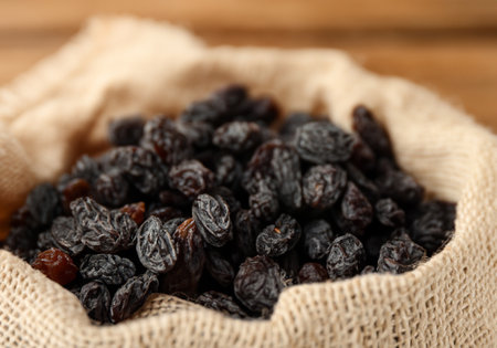 Black raisins in burlap bag over wooden tableの素材