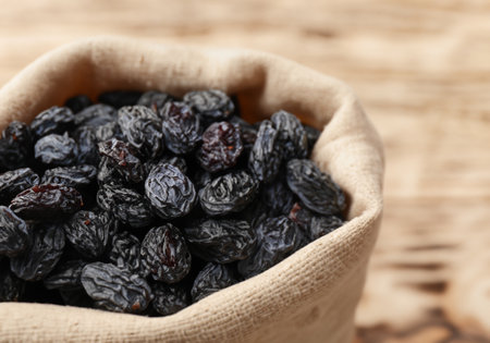 Black raisins in burlap bag over wooden tableの素材