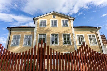 Vadstena, Sweden - May 23, 2021: Big yellow house in the corner of two streets with special red fence in the foregroundのeditorial素材