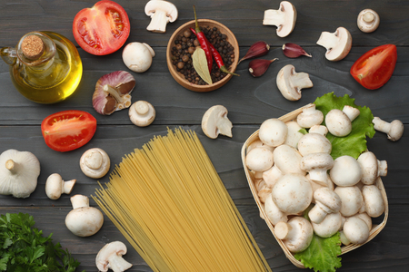 Italian food background, with tomatoes, parsley, spaghetti, mushrooms, oil, lemon, peppercorns on dark wooden table. Top viewの写真素材