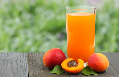 apricot juice on old wooden table with green garden backgroundの写真素材