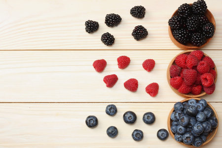 mix of blueberries, blackberries, raspberries in wooden bowl on light wooden table background. top...