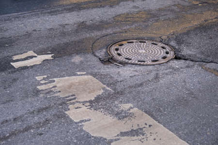An old sewer manhole cover surrounded by an asphalt streetの写真素材
