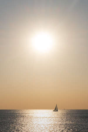 Orange colored seascape with sailboat over sunset skyの写真素材