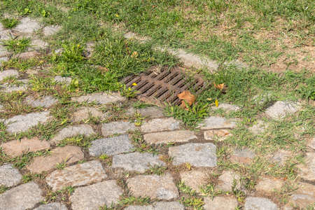 among the grass. cast iron rain drain on a street paved with granite stone. colored cobblestone road.の写真素材