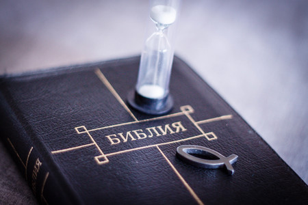 image of book Bible close-up in leather black binding with zipper with christian fish icon and hourglass on gray blurry background with black vignette.の写真素材