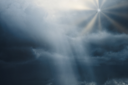 photograph of a cloudy sky with lead clouds and dim light hitting the clouds, and the bright rays of the sun from the clouds with a bird.の写真素材