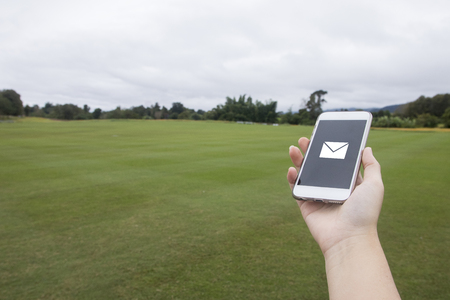 Hand hold mobile phone with email on screen, copy space, outdoor on grass field, business conceptの写真素材
