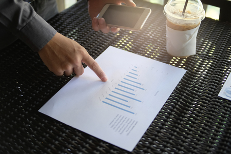 Business man holding cell phone and point at the paper of his business graph. business conceptの写真素材