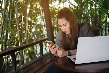 Woman used smartphone for business online with laptop on wooden table of brownの写真素材