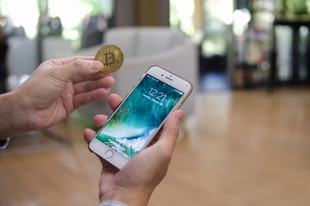 Chiang mai, Thailand - January 30 2017 : Man holding iphone 6 white color and BitCoin in blurred coffee cafe background, copy space for presentation productのeditorial素材