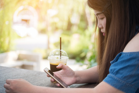 Close-up beautiful asian woman hold smartphone looking on screen in coffee cafeの写真素材