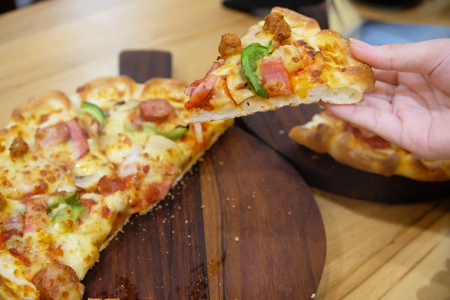 Close-up woman hand holding pizza slice, on wooden table of brown, fast foodの写真素材
