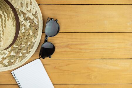 Eyeglasses and notepad with woven hat on wooden table of brown, travel and holiday conceptの写真素材