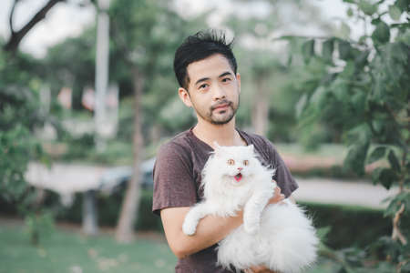 Man holding a beautiful furry Persian cat in the parkの写真素材