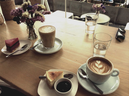 A cup of hot latte or cappuccino with cheesecake on the the wooden desk with retro filter effect