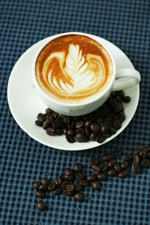 Cup of latte or cappuccino and coffee beans on blue table clothの写真素材