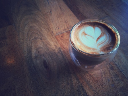 Latte or cappuccino coffee in small glass on wooden table at the cafe in retro filter effectの素材