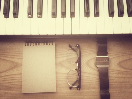 Music inspiration set with piano keyboard,notebook,watch and glasses on wooden desk in retro filter effectの素材