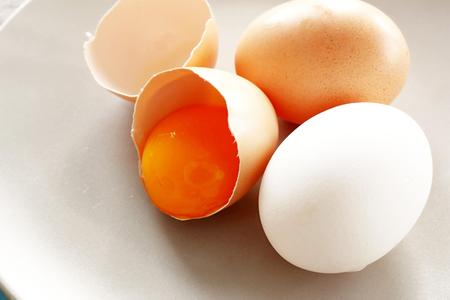 broken egg shell with yolk and untouched two eggs on plateの写真素材