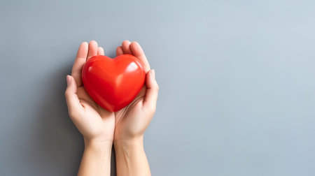 Female hands holding a red heart on a gray background with copy spaceの素材