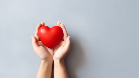Female hands holding a red heart on a gray background with copy spaceの素材