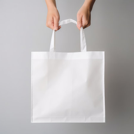 Female hand holding white paper shopping bag on gray background, mockup for designの素材