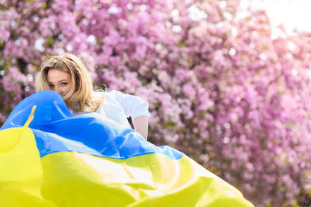 Beautiful blonde hair girl in a white shirt holds the flag of Ukraineの写真素材