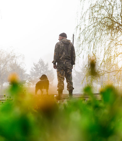 Hunter with a gun stands on the bridge with his dog Russian Spaniel