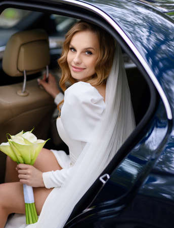 Beautiful caucasian blonde bride sitting in a stylish car with a bouquetの写真素材
