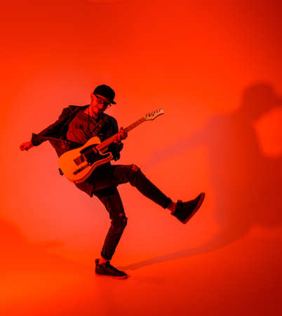 A young guitarist plays the electric guitar and jumps on a red lightの写真素材