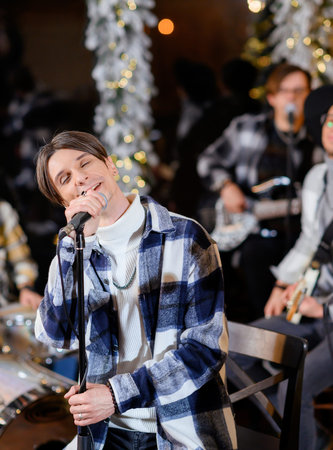 Young vocalist sings into a microphone on the background of a Christmas treeの写真素材