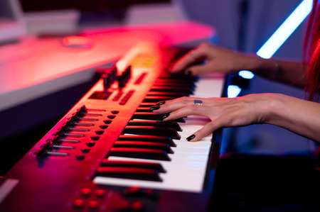 Female hands playing on synthesizer keys in a neon light recording studioの写真素材