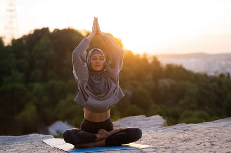 Beautiful young girl in a hijab meditates and practices yogaの写真素材