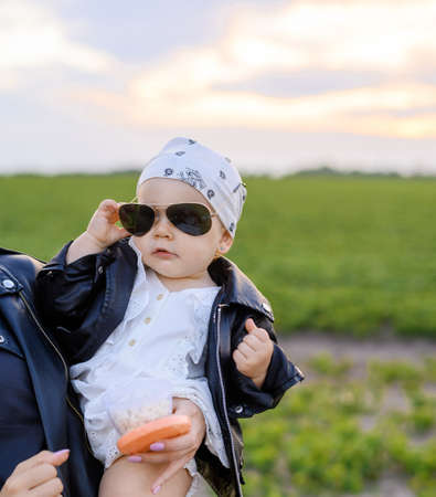 Little baby girl in sunglasses on the background of the sunset in the fieldの写真素材