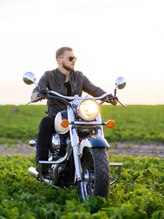 Young fair-haired brutal biker guy with a beard in sunglasses on a motorcycle