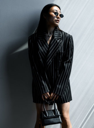 Beautiful Asian girl in black striped jacket wearing sunglasses posingの写真素材