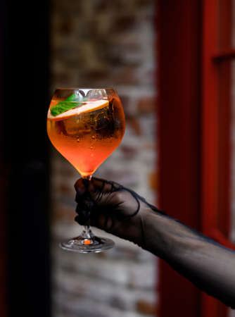 A female hand in black gloves holds a glass of Aperol cocktailの写真素材
