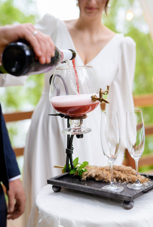 A beautiful newlywed couple pours champagne into a vessel