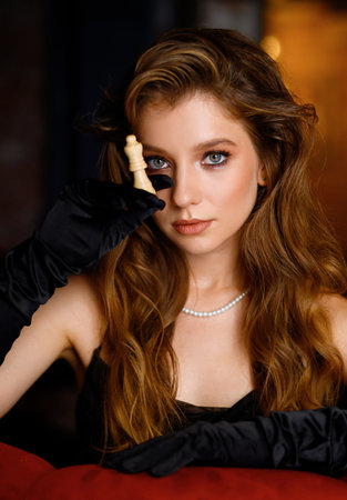 A beautiful Caucasian girl in a black dress poses with a chess piece