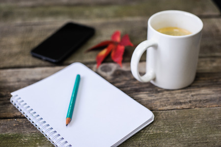 smartphone, a notebook for writing, a book and a cup of coffee, frame composition on vintage board backgroundの写真素材