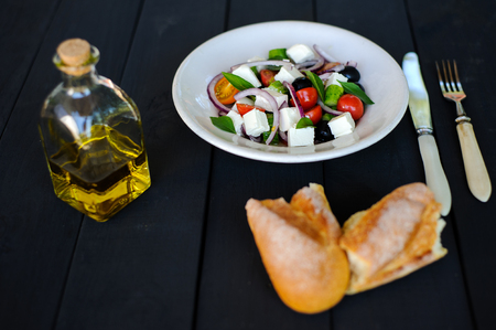 fresh and healthy vegetable mediterranean salad with feta cheese, cucumber, tomato, olives and red onion bulbs. ingredients and fresh baked homemade greek country bread on background, close-upの写真素材