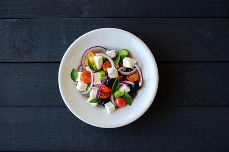 fresh and healthy vegetable mediterranean salad with feta cheese, cucumber, tomato, olives and red onion bulbs. ingredients and fresh baked homemade greek country bread on background, close-upの写真素材