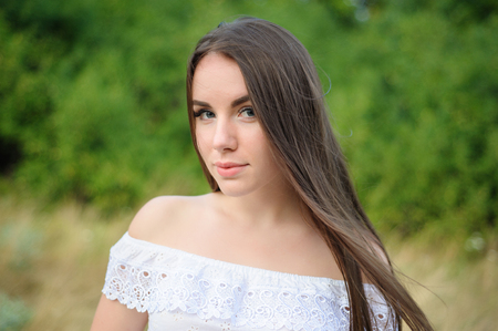 portrait of a young beautiful girl in a park in white dressの写真素材