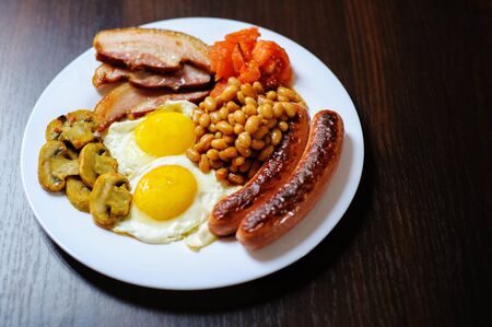 Traditional English or Irish breakfast: sausages, bacon, egg, mushrooms, tomatoes and toasts. Nutritious morning meal. horizontalの写真素材