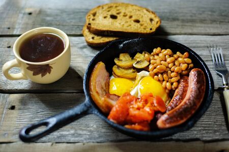 full irish breakfast with fried egg, sausages, black pudding, white pudding, baked beans, bacon, tomato and grilled mushrooms in a cast iron panの写真素材