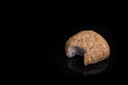 Fresh, bitten roll with grains isolated on black reflective surfaceの写真素材