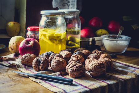 Whole raw walnurs on the table covered with dusters and jars with preserves, apples and sugarの写真素材
